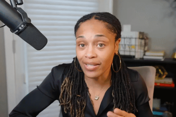 Presenter looking directly at camera, speaking with a focused expression; microphone visible at left.