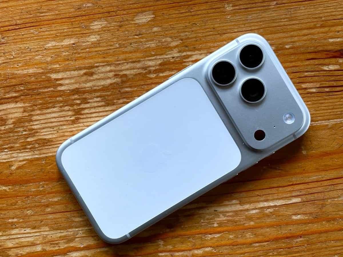 Back of a silver iPhone 17 Pro showing its triple camera plateau, lying on a wooden table