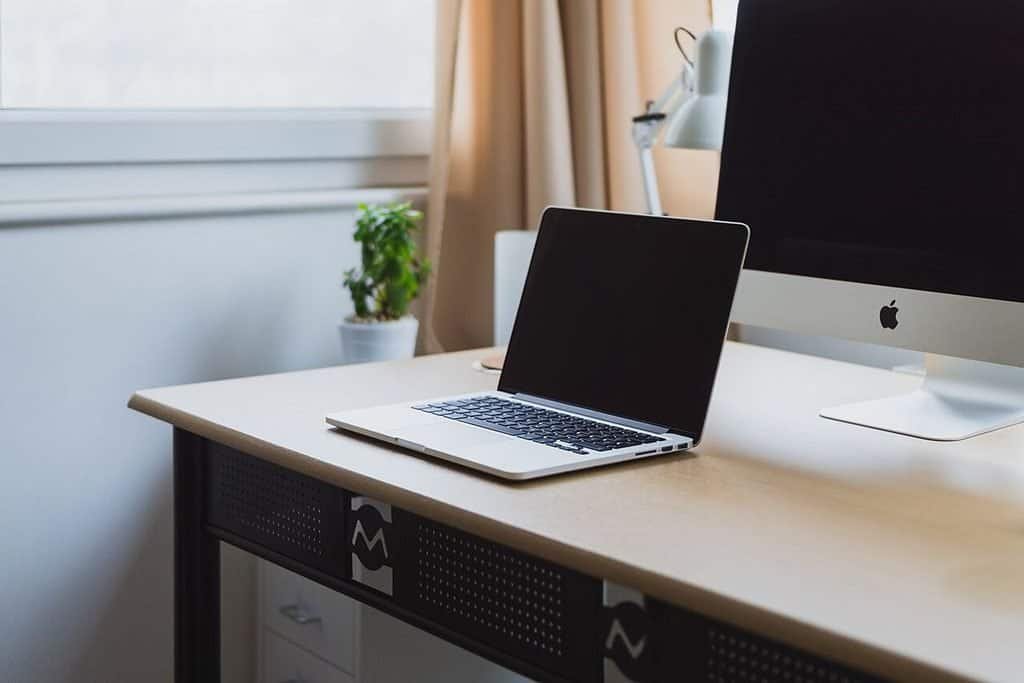 Laptop open on a clean white desk next to a desktop monitor