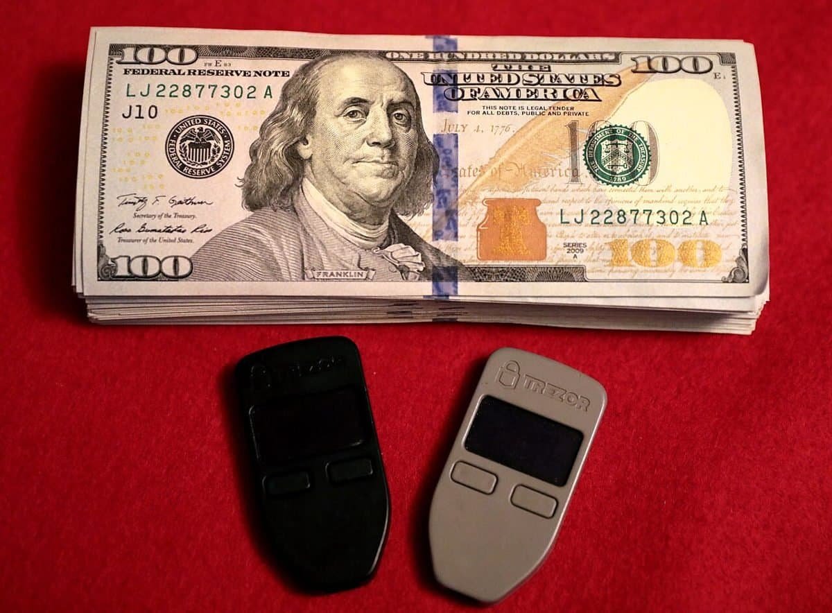 Two Trezor hardware wallets next to a stack of US dollar bills