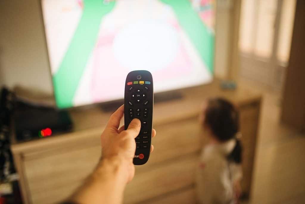 Adult pointing a remote at a TV while a child watches from the floor
