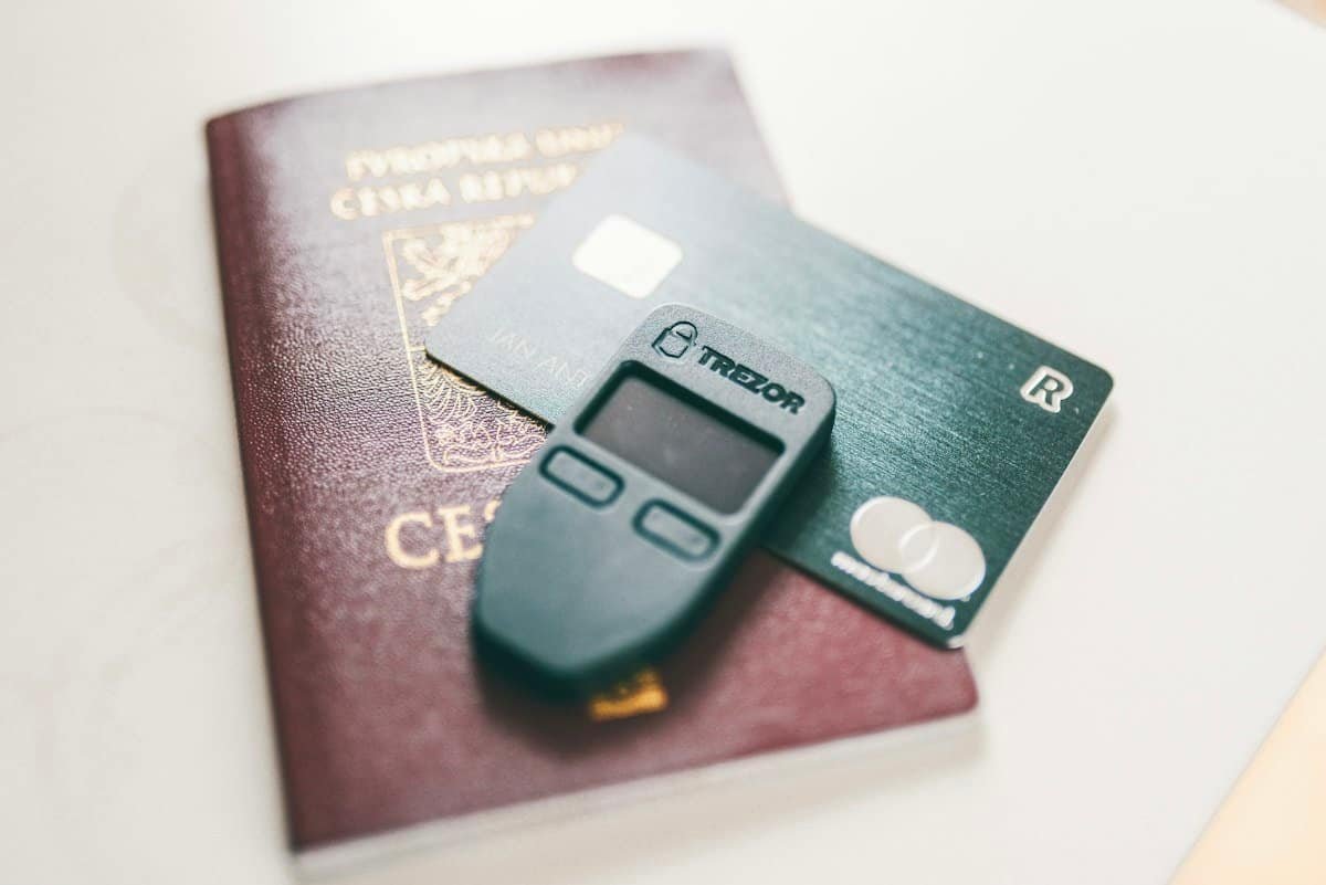 Black Trezor hardware crypto wallet resting on a bank card and a passport