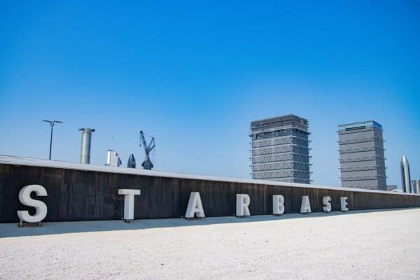 The STARBASE sign beside Texas State Highway 4, with Starship hardware and SpaceX's tall assembly buildings in the background