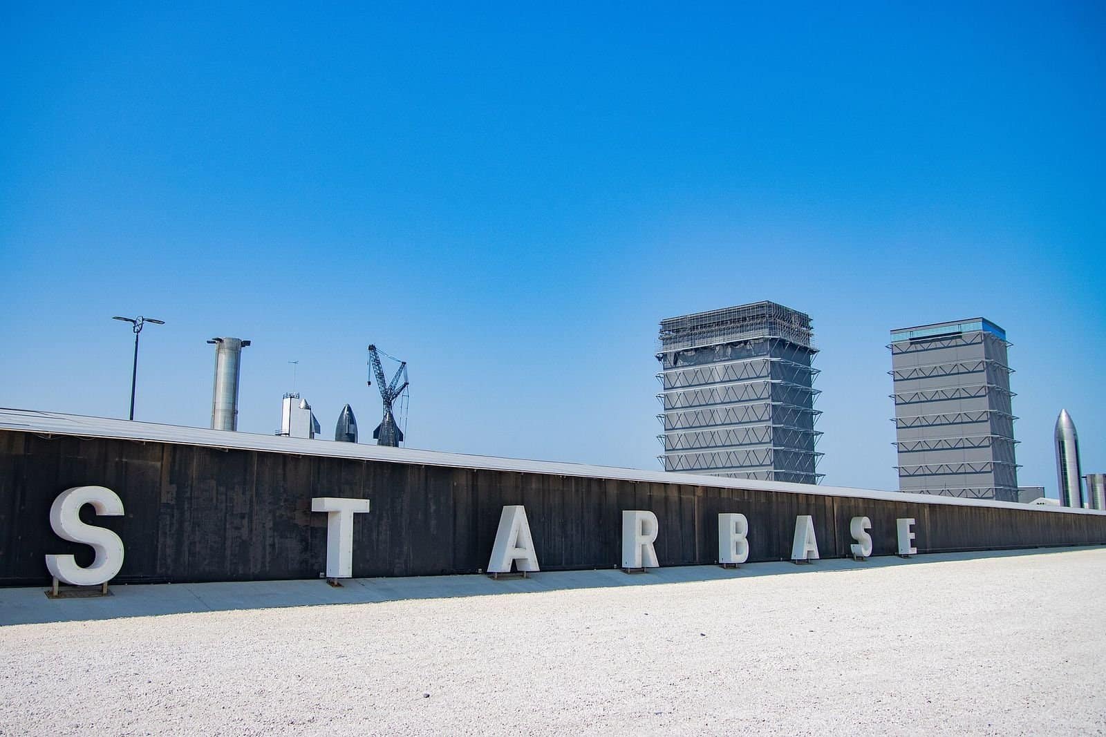 The STARBASE sign beside Texas State Highway 4, with Starship hardware and SpaceX's tall assembly buildings in the background