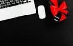Laptop and wireless mouse beside a black gift box with a red bow and a Black Friday tag