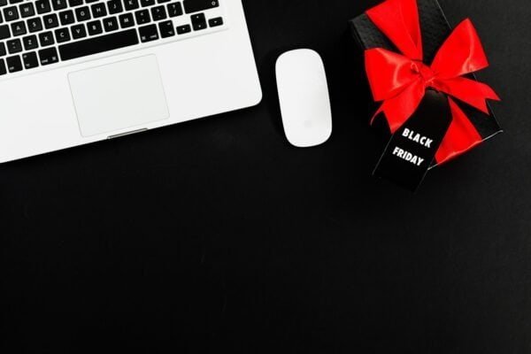 Laptop and wireless mouse beside a black gift box with a red bow and a Black Friday tag